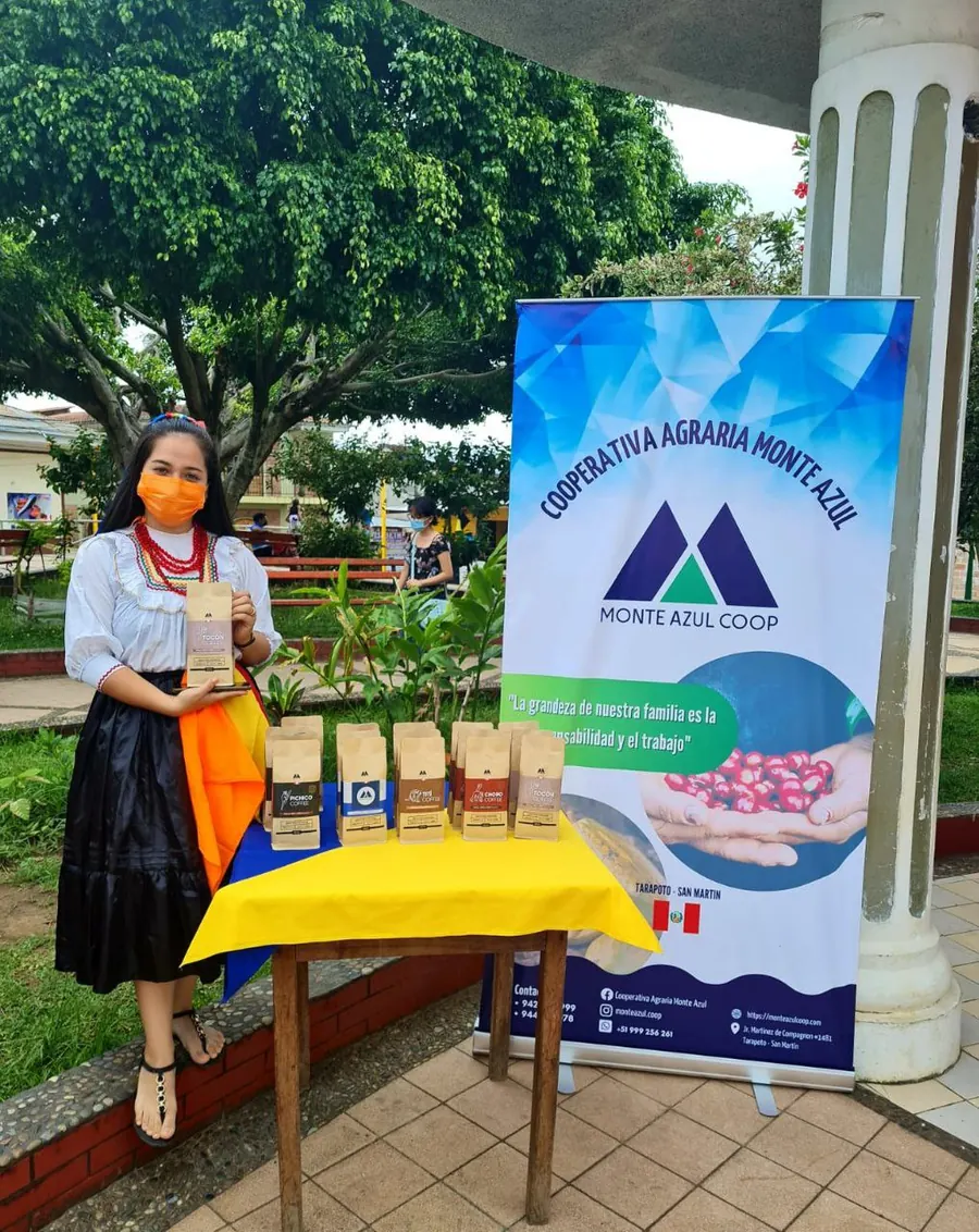 Socia de la cooperativa con productos de Monte Azul junto al banner de la cooperativa