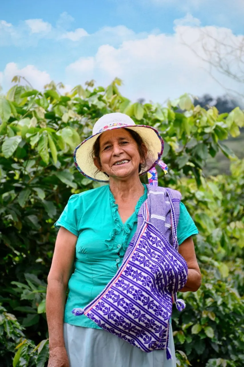 Socia de la cooperativa con un bolso tejido entre cafetos